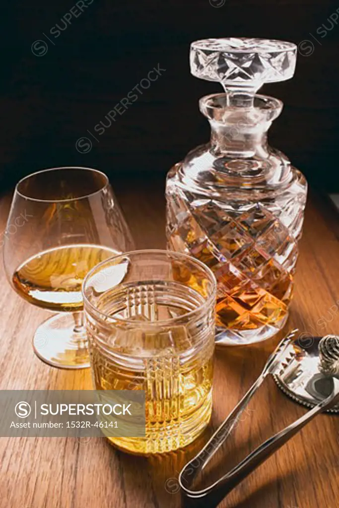 Cognac & whisky in glasses & carafe, ice tongs beside them