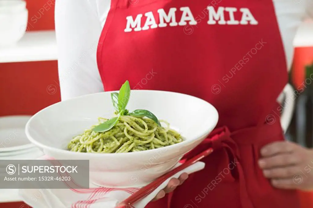 Woman in red apron holding plate of spaghetti with pesto