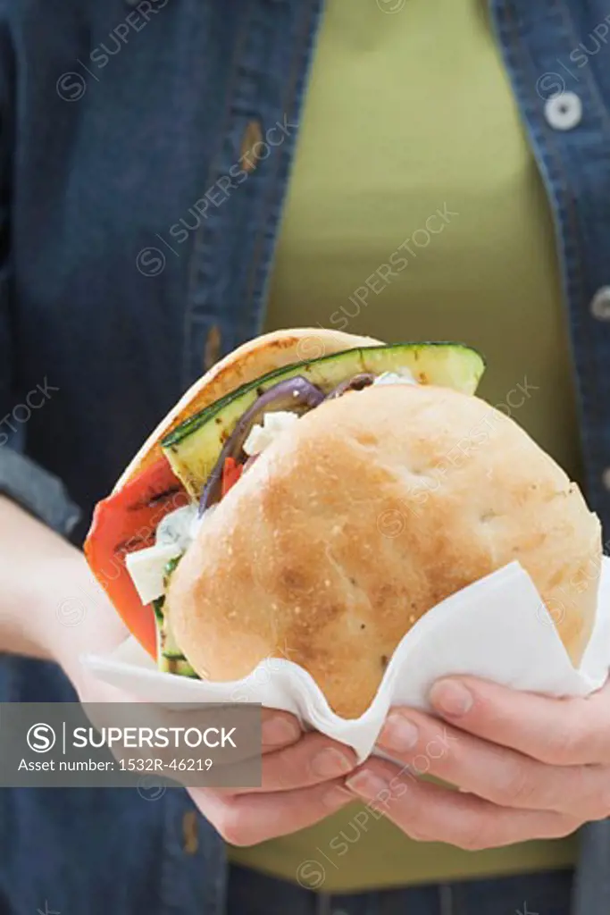 Woman holding toasted roll filled with grilled vegetables