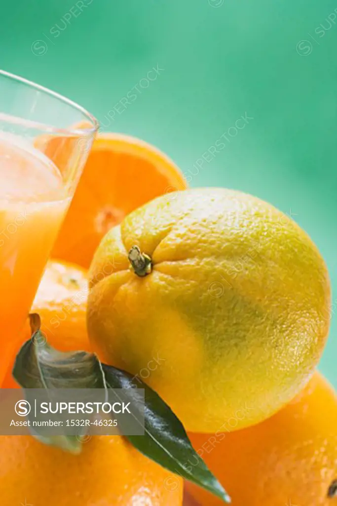 Several oranges beside glass of orange juice