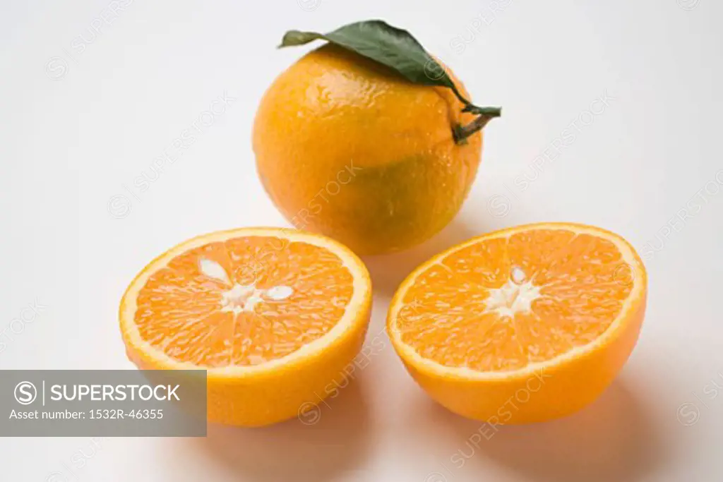 Two orange halves in front of whole orange with leaf