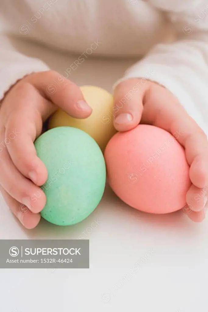 Child's hands holding three coloured eggs