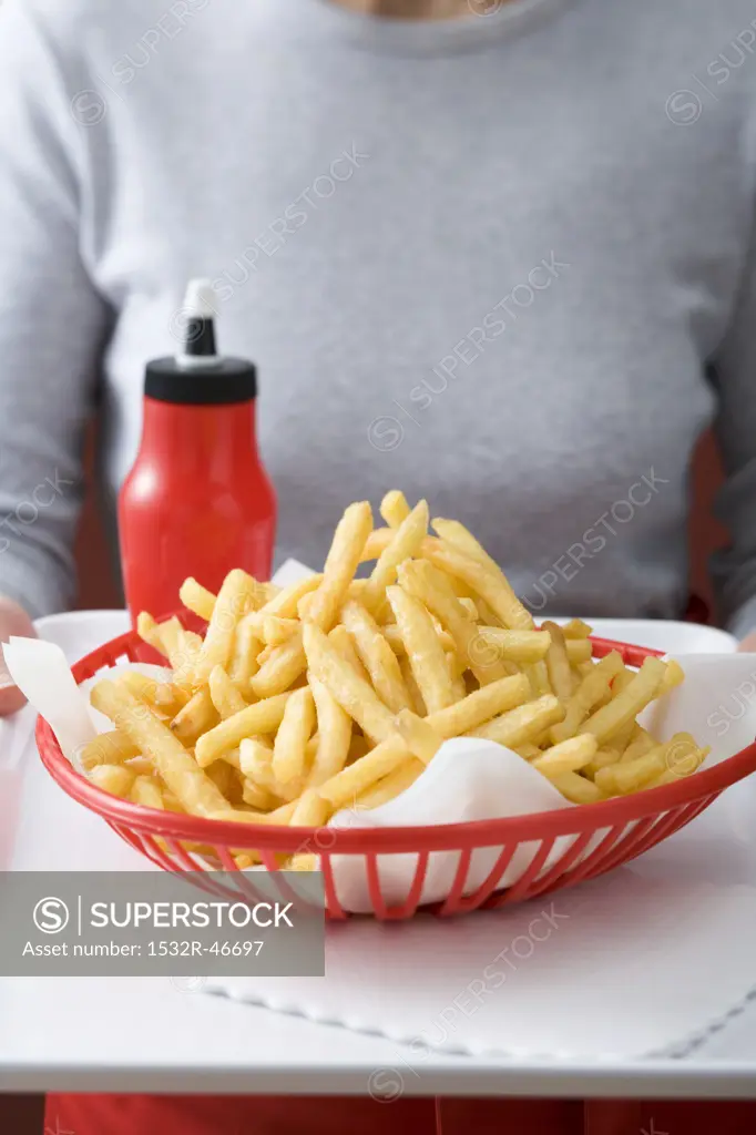 Chips in plastic basket, ketchup, woman in background