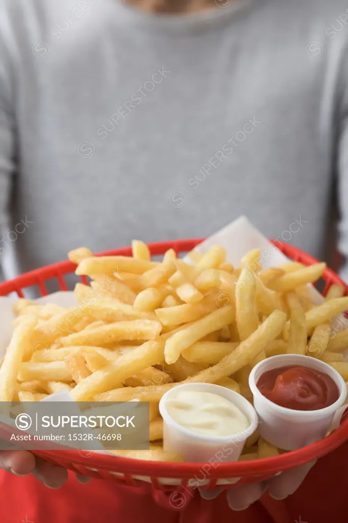 Woman holding basket of chips with ketchup and mayonnaise