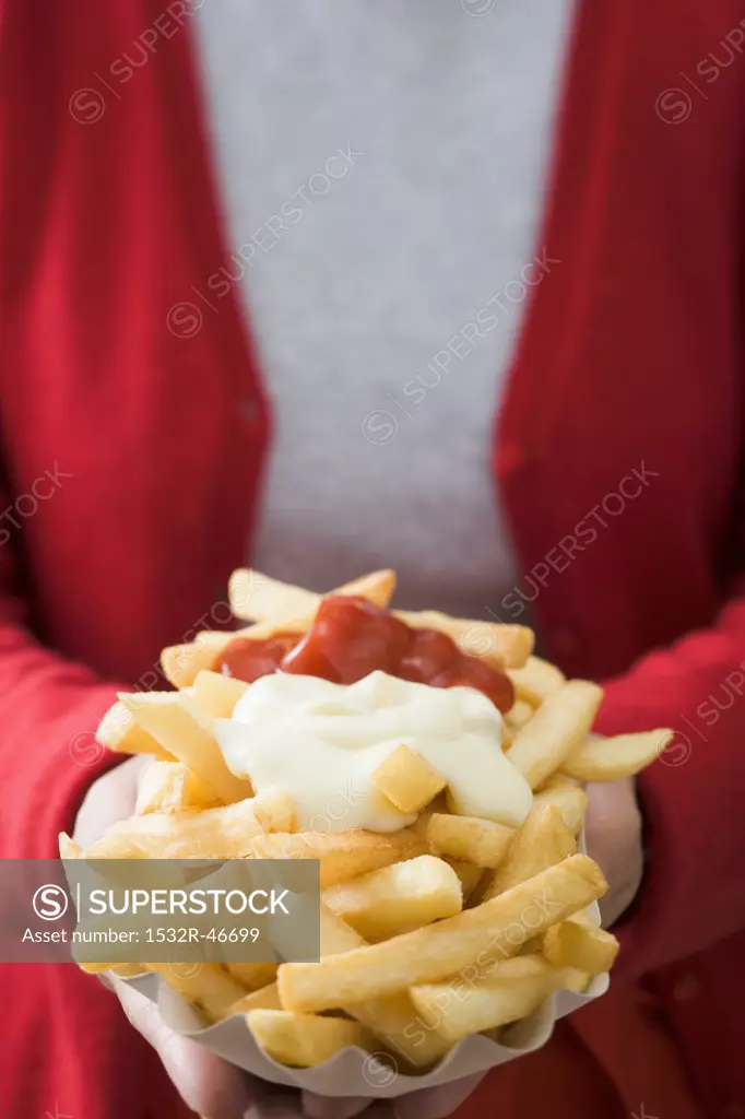 Woman holding paper dish of chips with ketchup & mayonnaise
