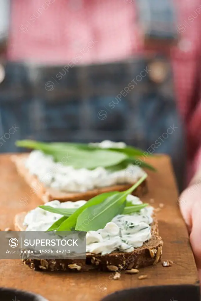 Person holding wholemeal bread with quark & ramsons on board