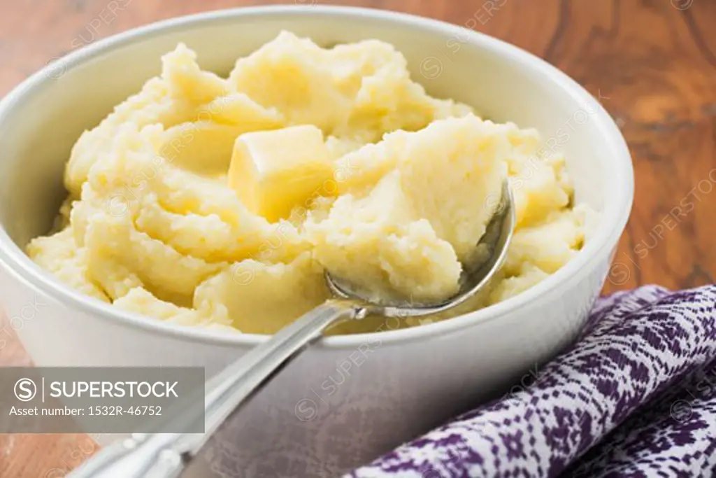 Mashed potato with butter in white bowl with spoon