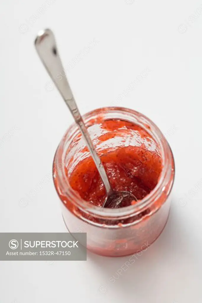 Jam jar with spoon and remains of strawberry jam