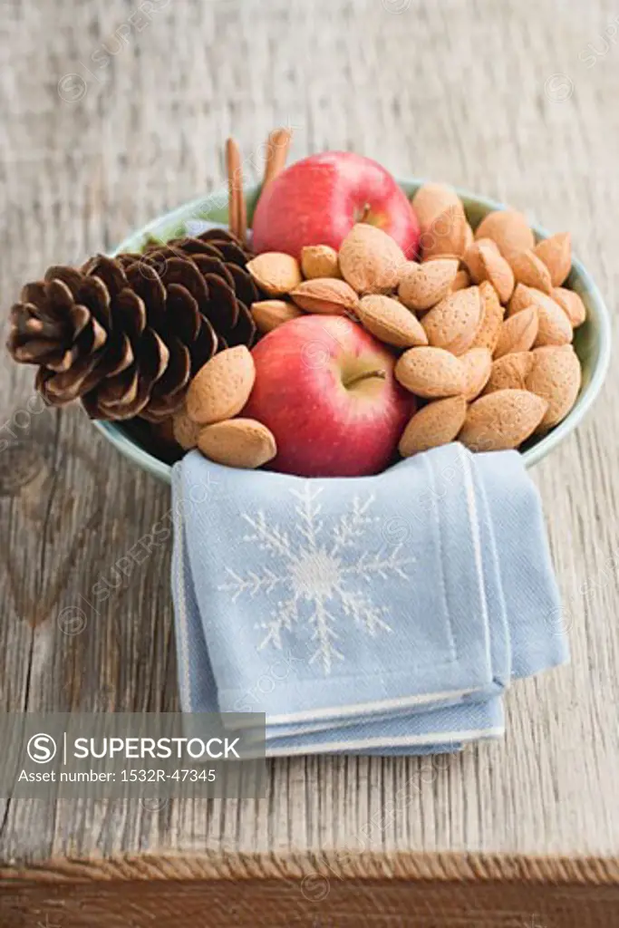 Red apples, almonds and cone in bowl on wooden table
