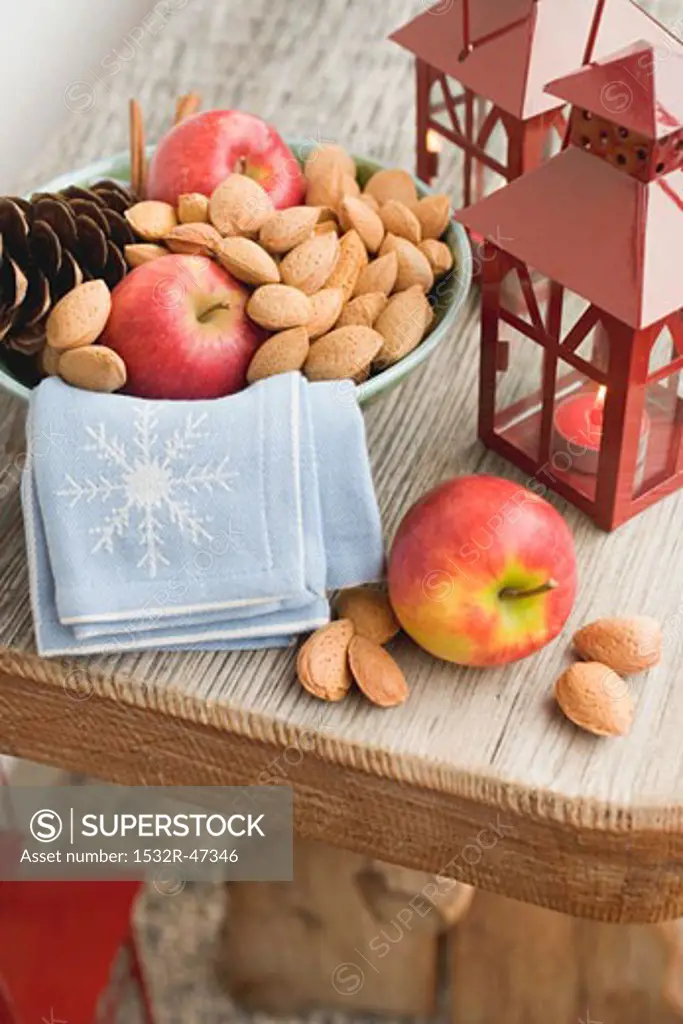 Red apples, almonds and cone in bowl, lanterns beside it