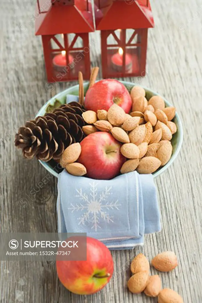 Red apples, almonds and cone in bowl in front of lanterns
