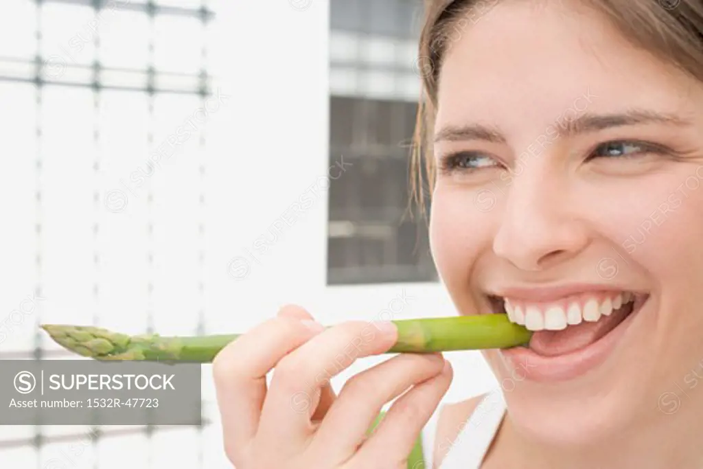 Young woman biting into a spear of green asparagus