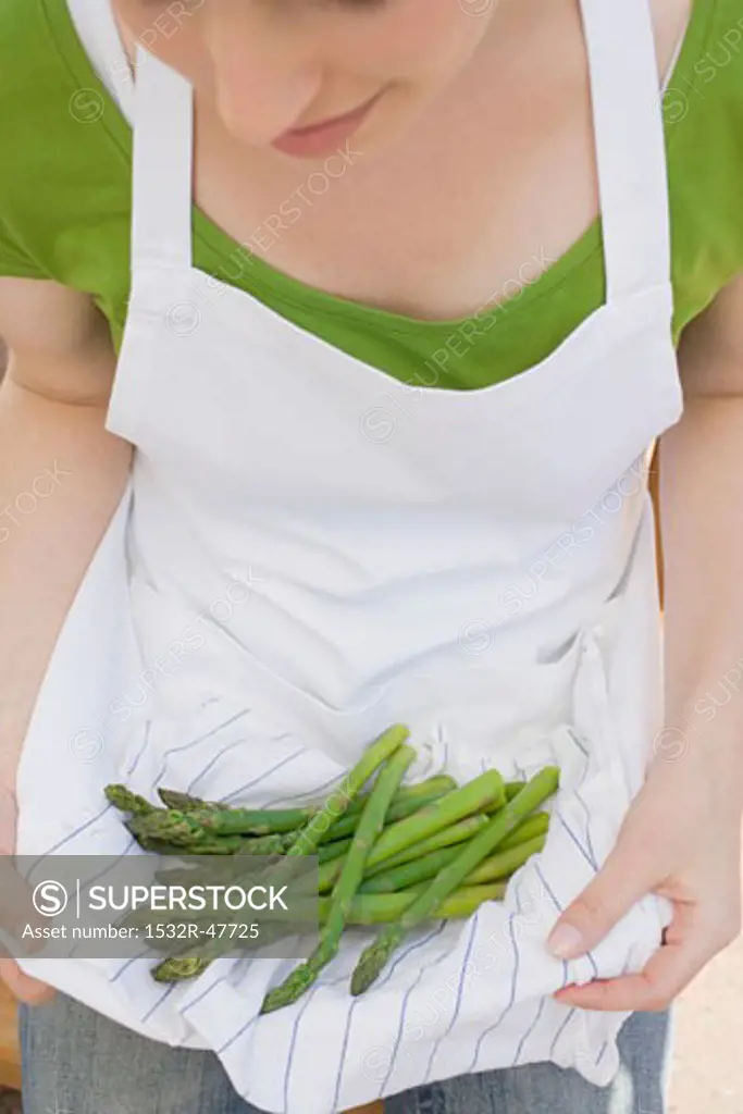 Young woman holding green asparagus in her apron