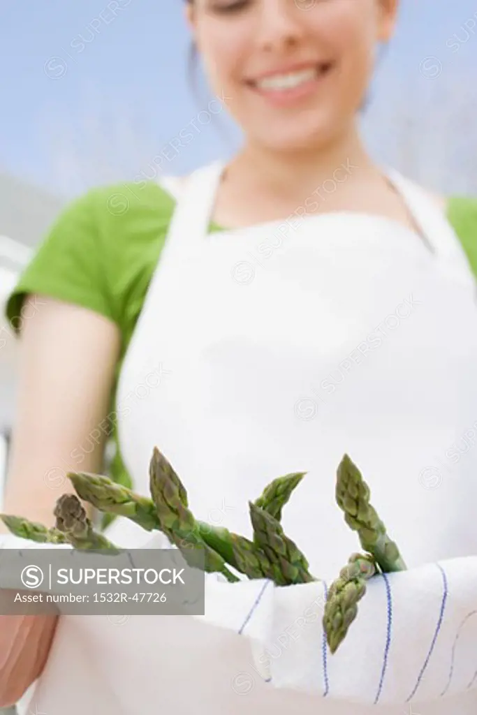 Young woman holding green asparagus in her apron