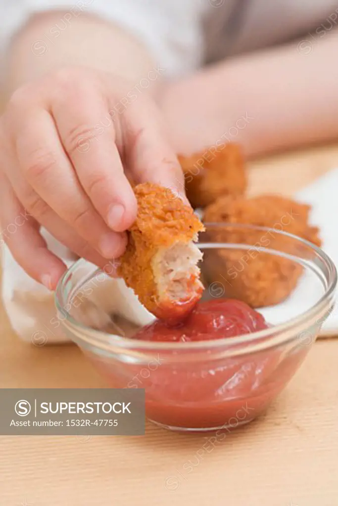 Child dipping chicken nugget in ketchup
