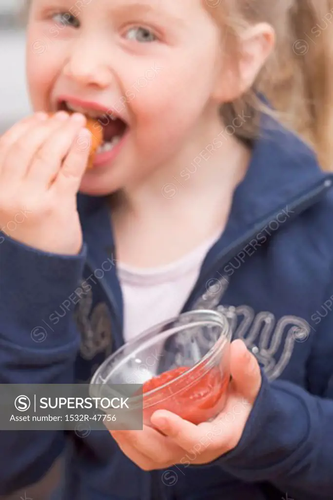 Little girl eating chicken nugget with ketchup