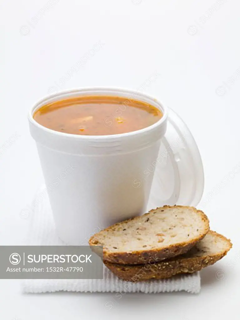 Tomato & vegetable soup in polystyrene cup, bread beside it