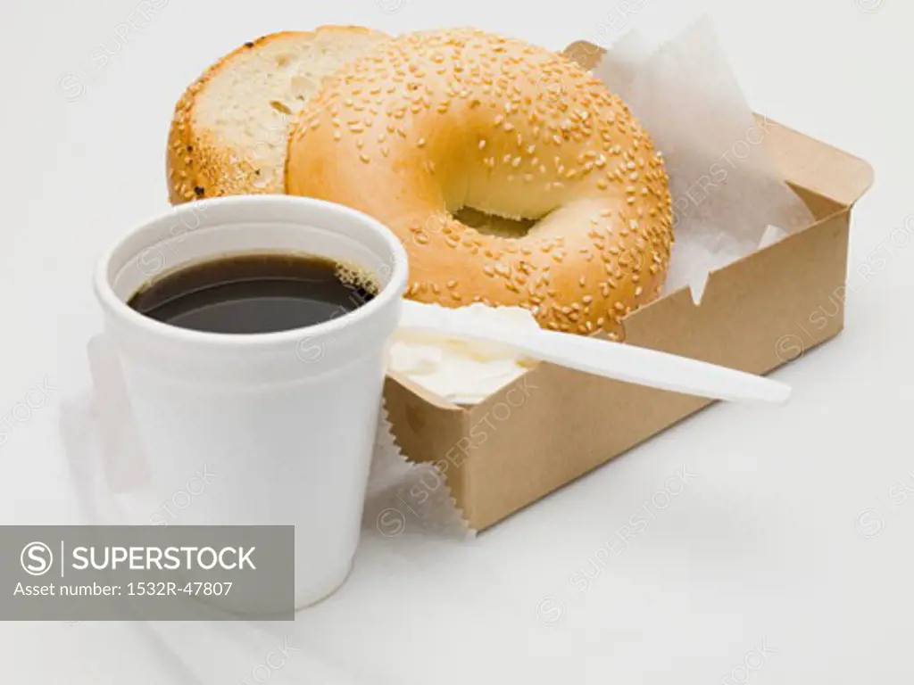 Sesame bagel with crème fraîche in cardboard box, cup of coffee