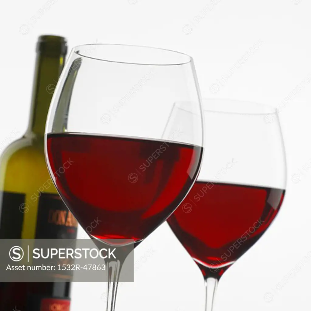 Two glasses of red wine in front of bottle