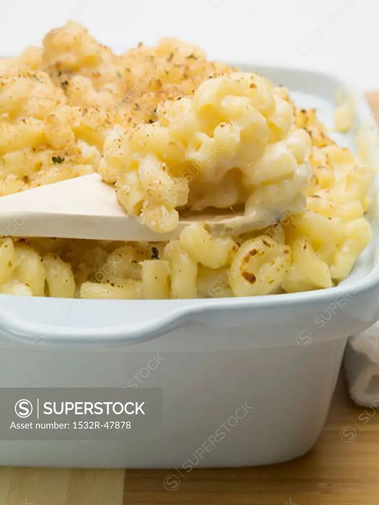 Macaroni cheese in baking dish with wooden spoon