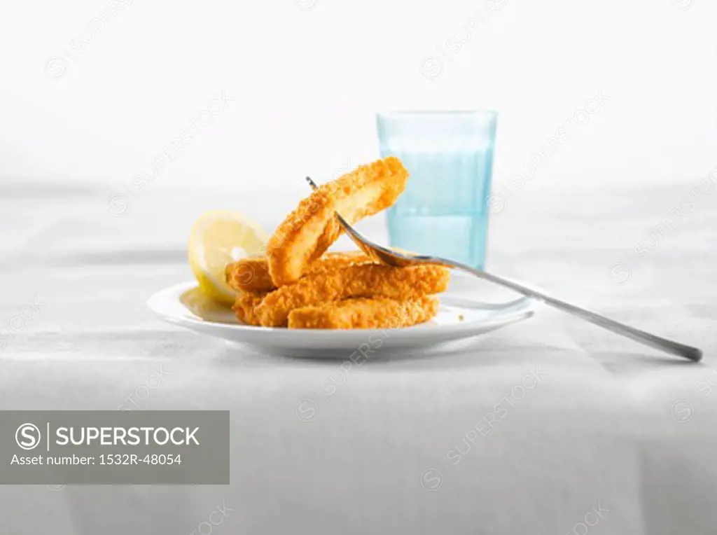 Fish fingers with lemon on plate, glass of water