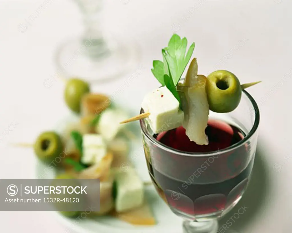 Feta, olive & halibut on cocktail stick on glass of red wine
