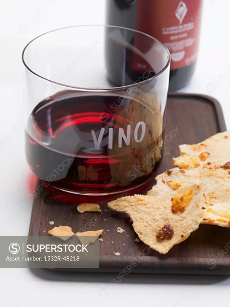 Glass of red wine and crackers on tray, bottle of red wine