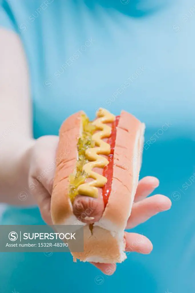 Woman holding hot dog with mustard, relish and ketchup
