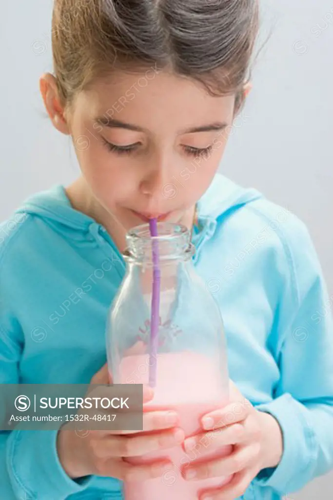 Little girl drinking strawberry milk out of bottle with straw