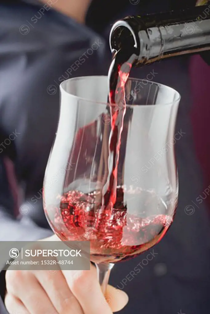 Person pouring red wine into a glass