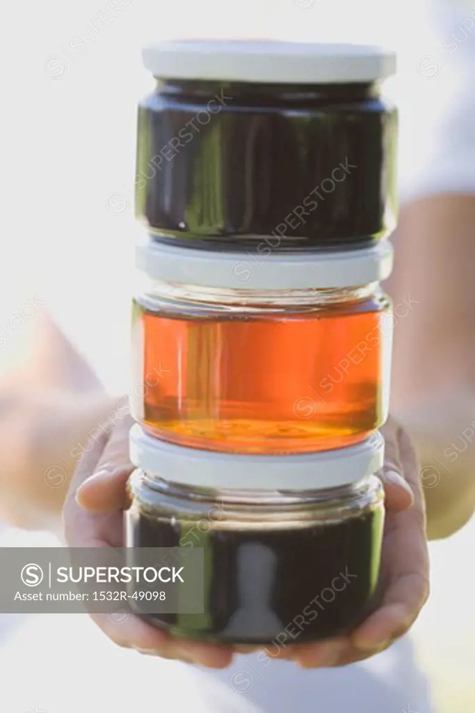 Hands holding three jars of honey