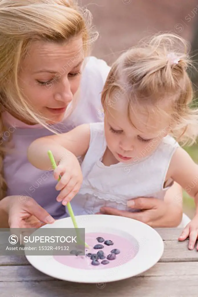 Little girl stirring blueberry yoghurt with spoon