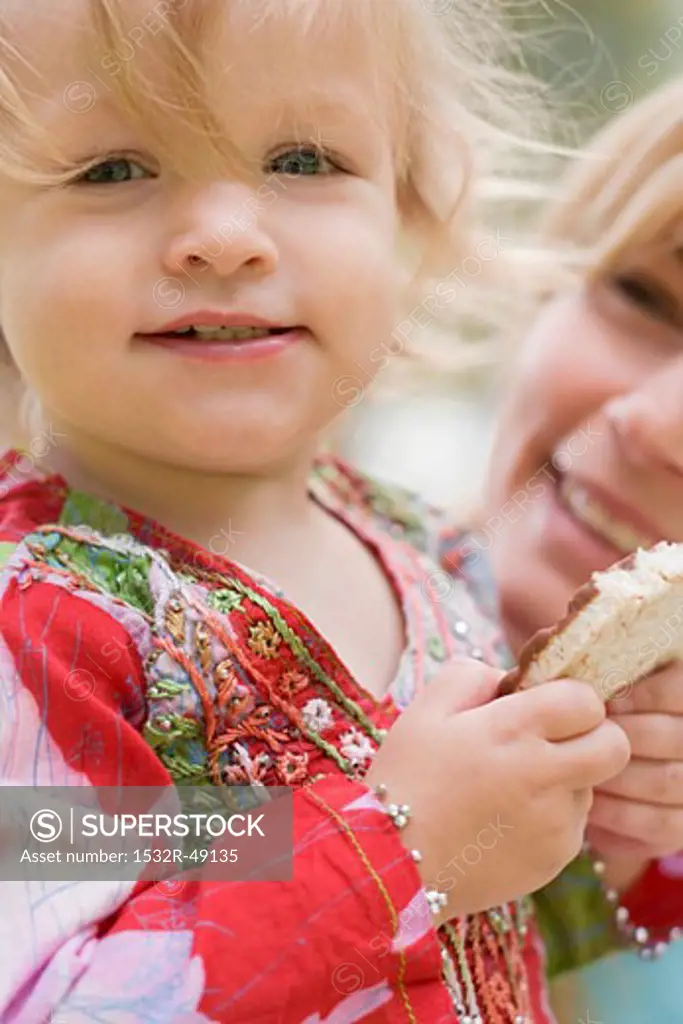 Little girl eating rice cake, woman in background