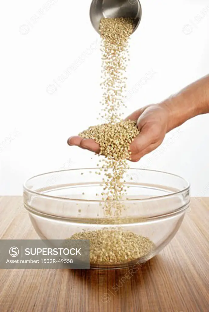 Someone pouring buckwheat over their hand into a glass bowl