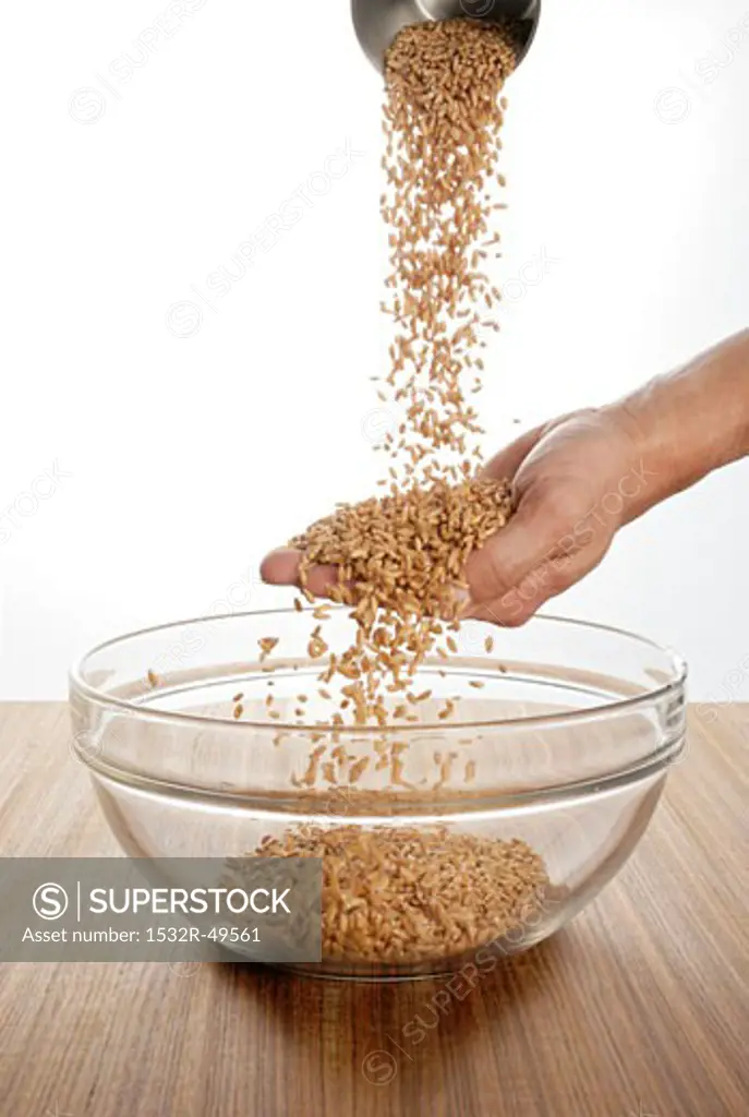 Someone pouring spelt over their hand into a glass bowl