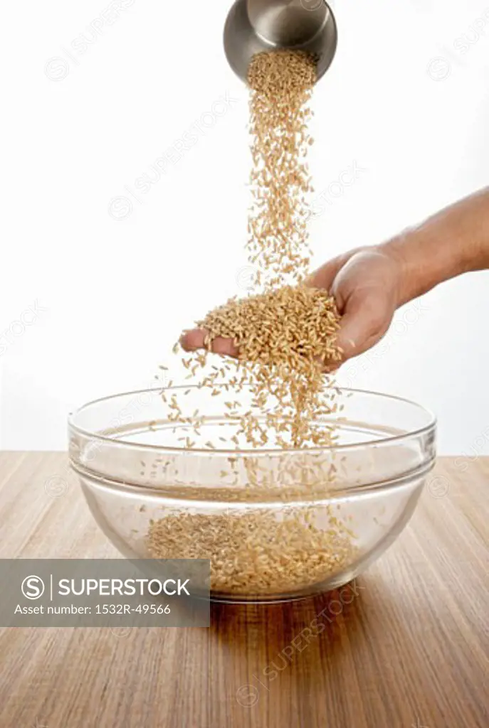 Someone pouring oats over their hand into a glass bowl