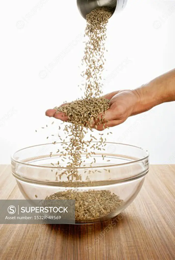 Someone pouring rye over their hand into a glass bowl