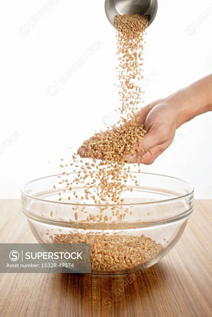Someone pouring wheat over their hand into a glass bowl