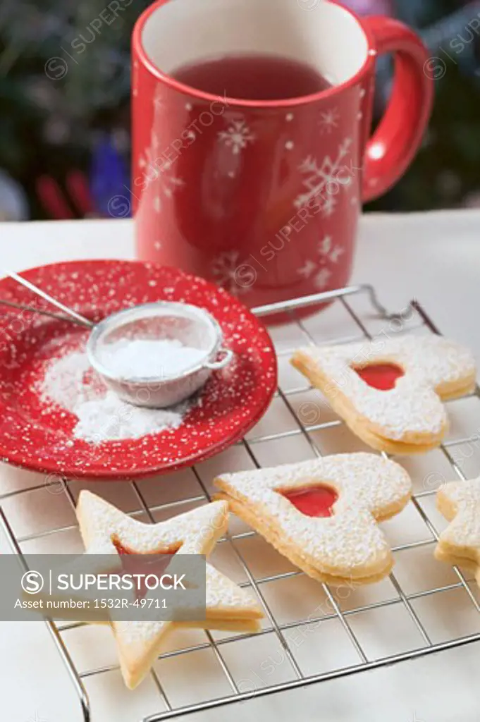 Jam biscuits on cake rack, icing sugar, mug of tea