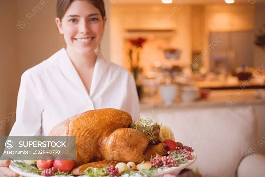 Young woman serving roast turkey on platter