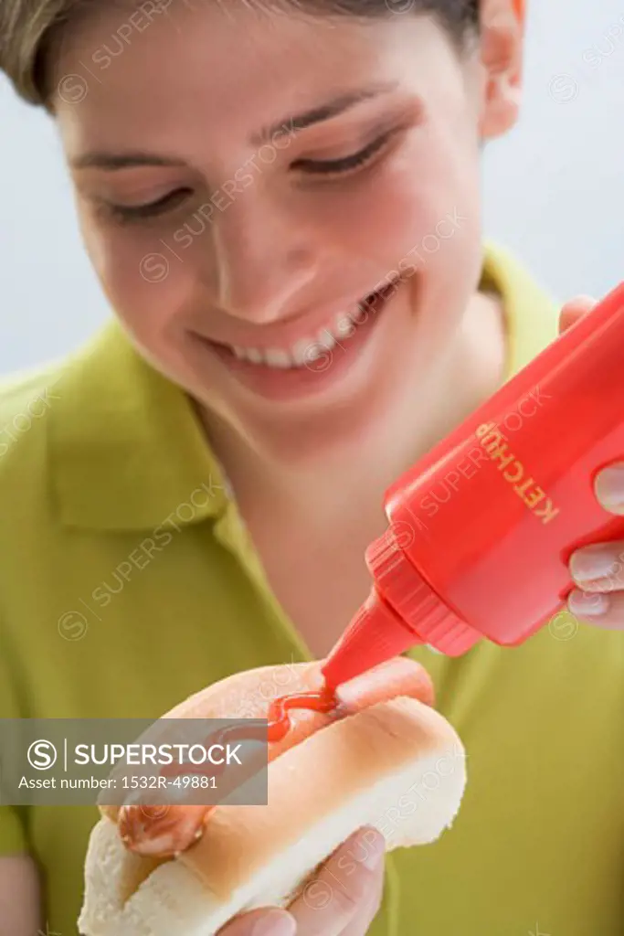 Young woman putting ketchup on hot dog