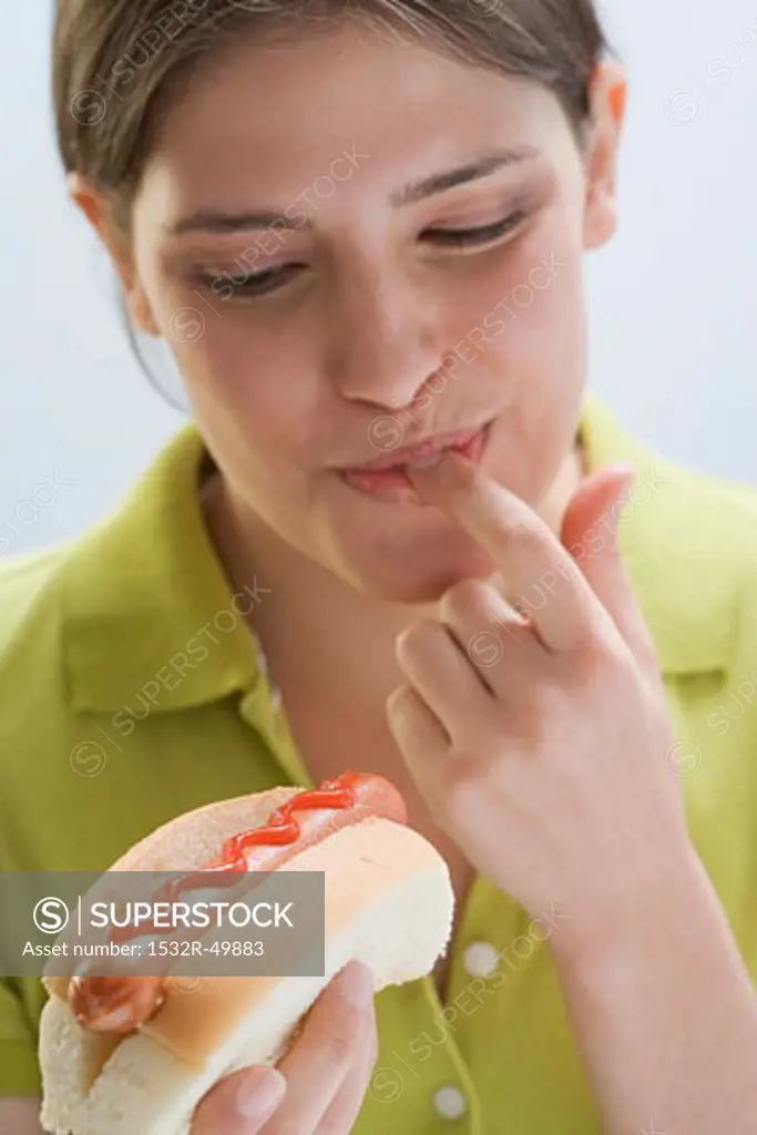 Young woman tasting ketchup on hot dog