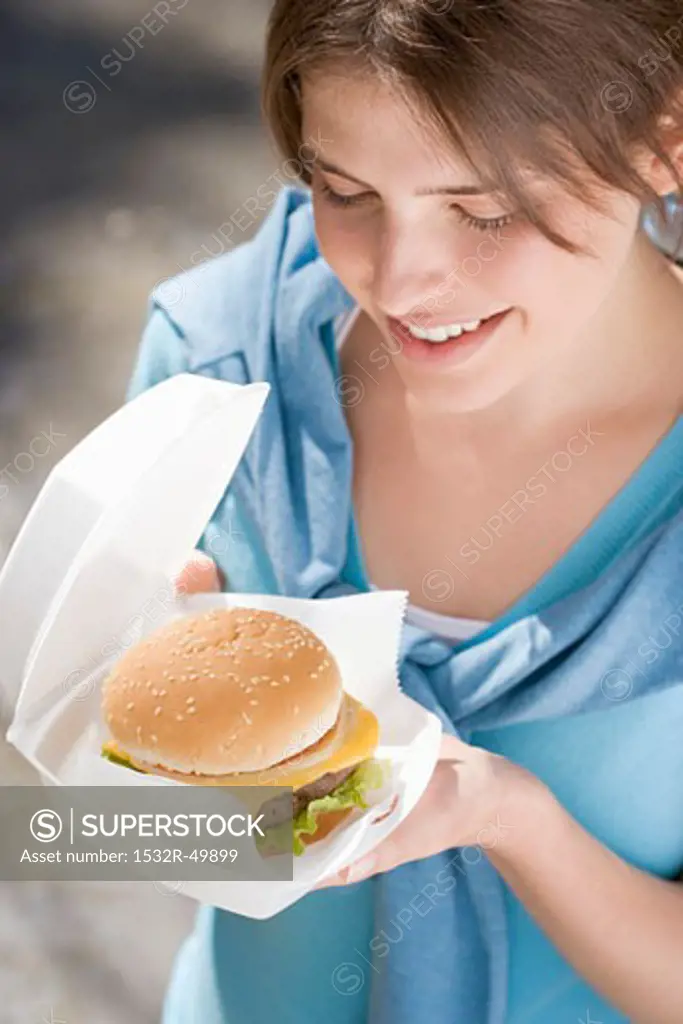 Young woman with cheeseburger out of doors