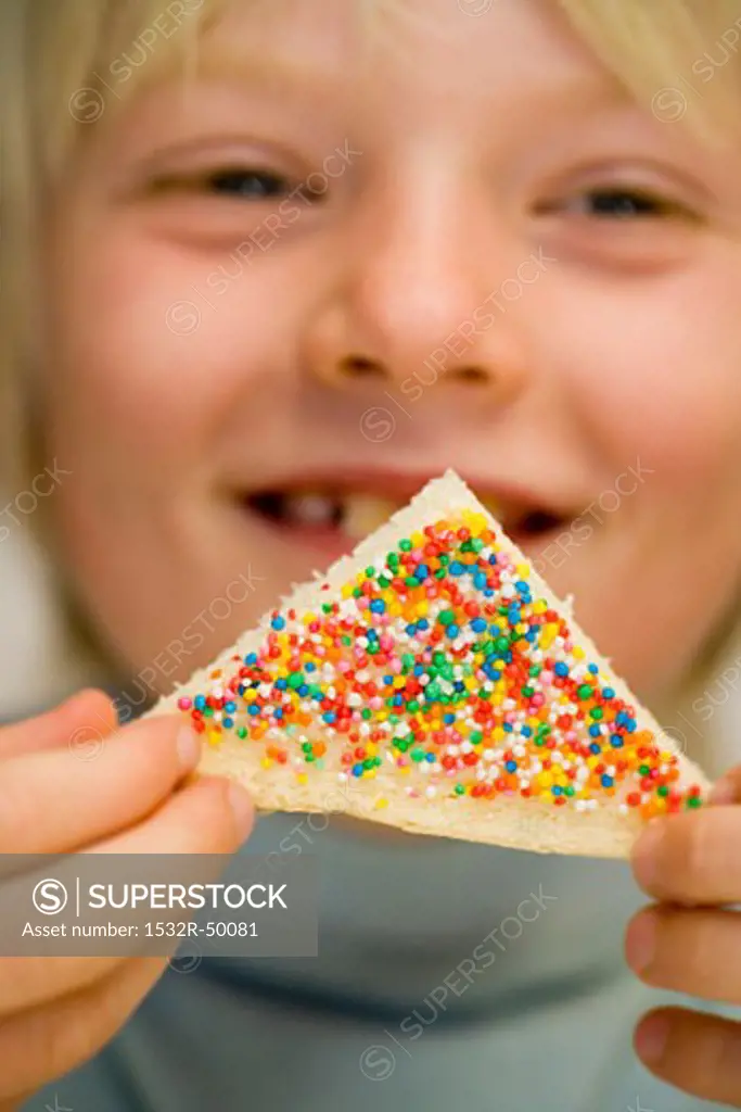 Boy holding fairy bread (Bread triangle with sprinkles, Australia)