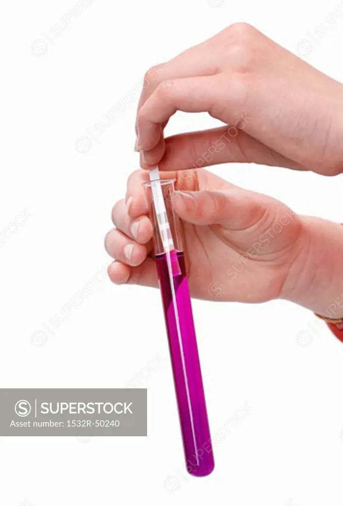 Hands holding litmus paper in test-tube