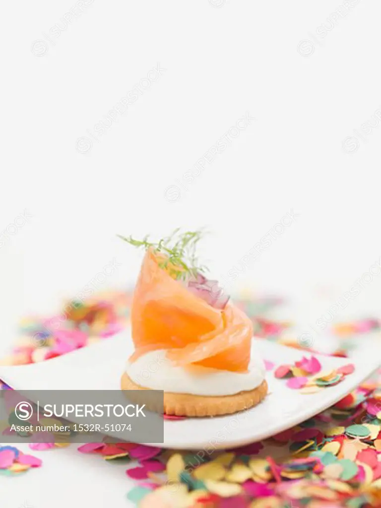 Smoked salmon on cracker on plate surrounded by confetti