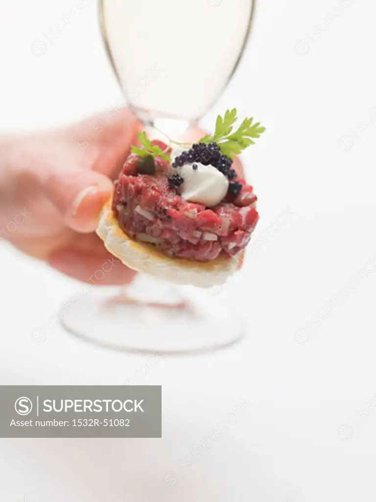 Hand holding sparkling wine glass and tuna tartare canapé