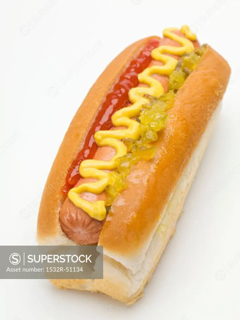 A hot dog with ketchup, mustard and gherkin