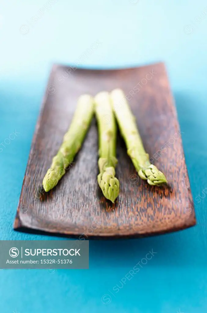 Three spears of green asparagus in wooden dish