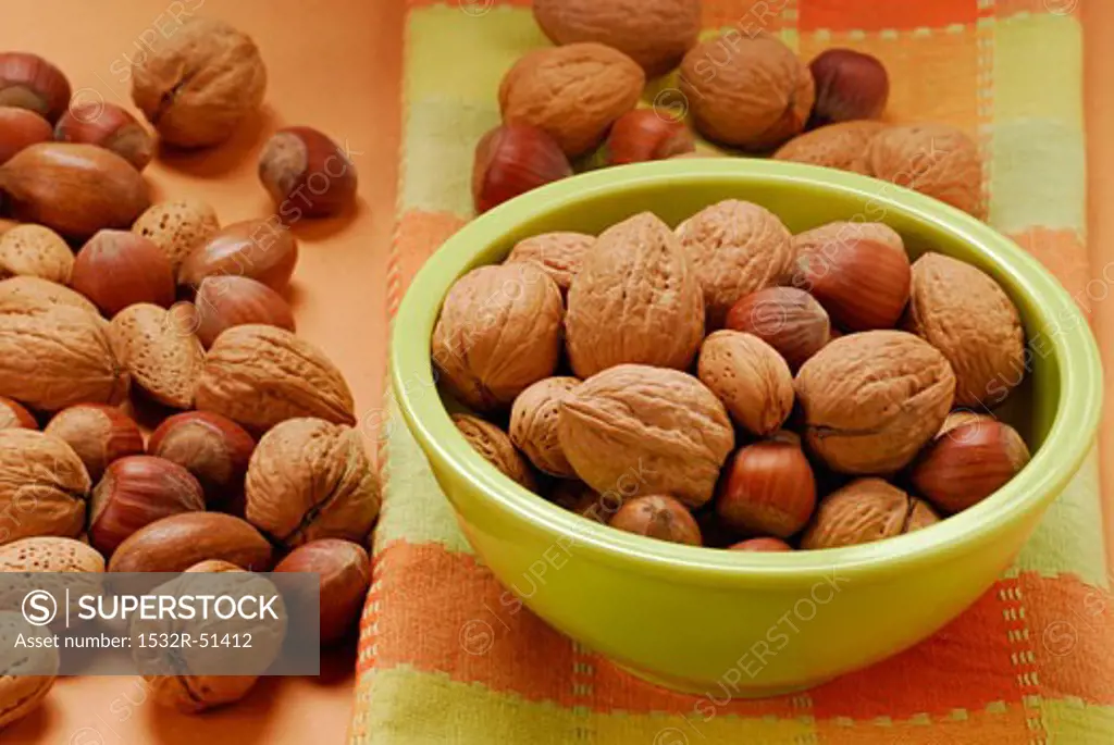 Unshelled walnuts, hazelnuts and almonds in green bowl